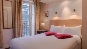 A hotel room with a large bed, a bedside table with a lamp, a framed picture on the wall, and a window with curtains. - Hôtel Gaillon Opéra (Paris)