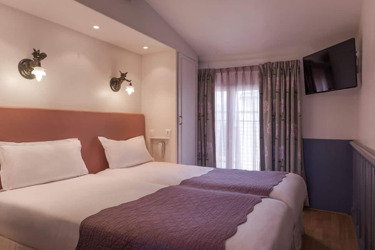 Una habitación de hotel con dos camas, un televisor montado en la pared y una ventana con cortinas.