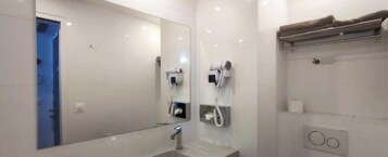 Un bagno moderno con uno specchio grande, due asciugacapelli montati a parete, un porta asciugamani e un porta carta igienica.