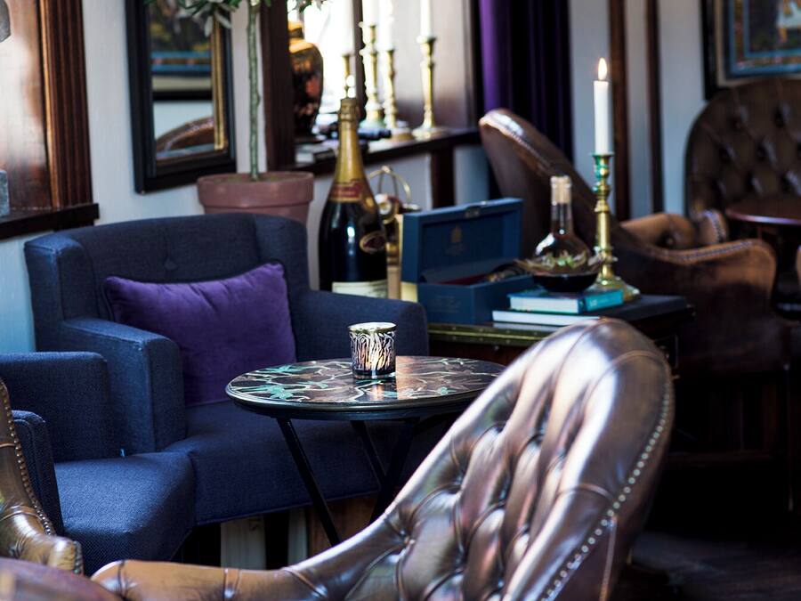 A cozy seating area with a leather armchair, a blue sofa, and a small round table with a candle and a bottle.
