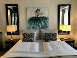 Un cuarto de hotel con una cama grande, dos mesitas de noche con lámparas, un cuadro en la pared y dos espejos.
