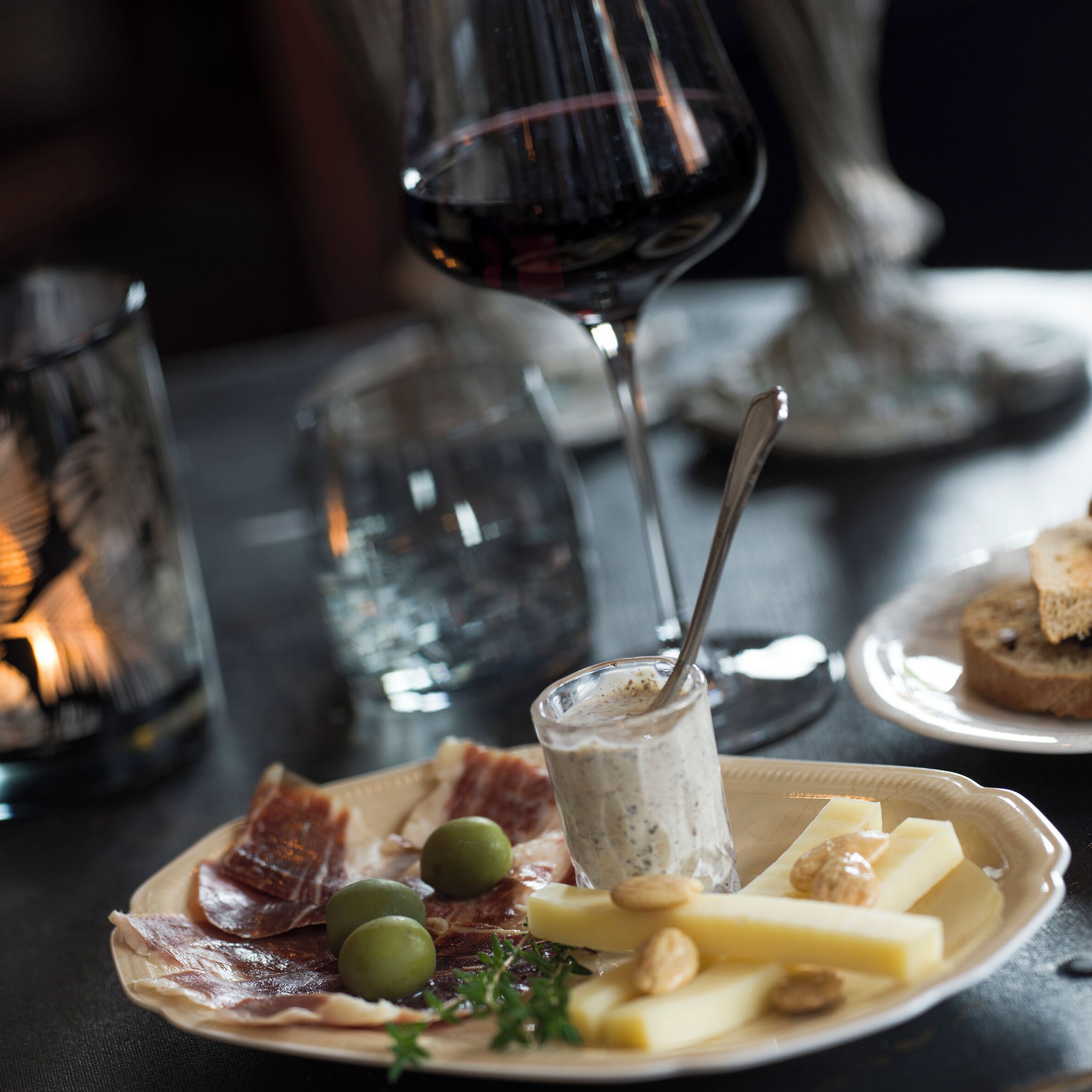 A plate of cheese, olives, and nuts with a glass of red wine and a spoon.