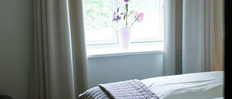 A hotel room with a bed, a window with curtains, and a vase with flowers.