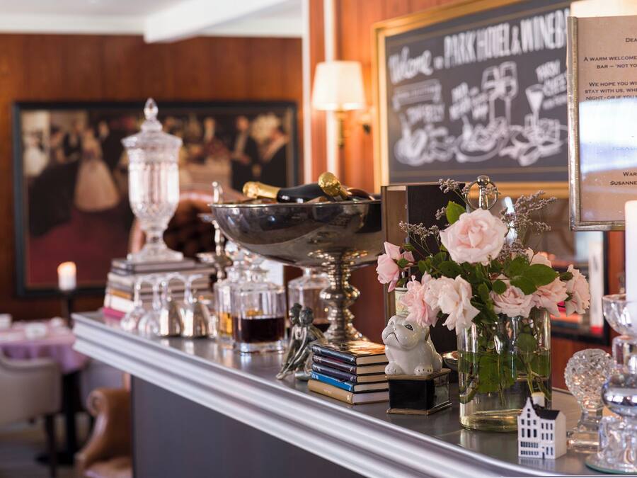 Una zona de bar con un menú en una pizarra, un cuenco decorativo, libros, un jarrón con flores y un pequeño modelo de casa.