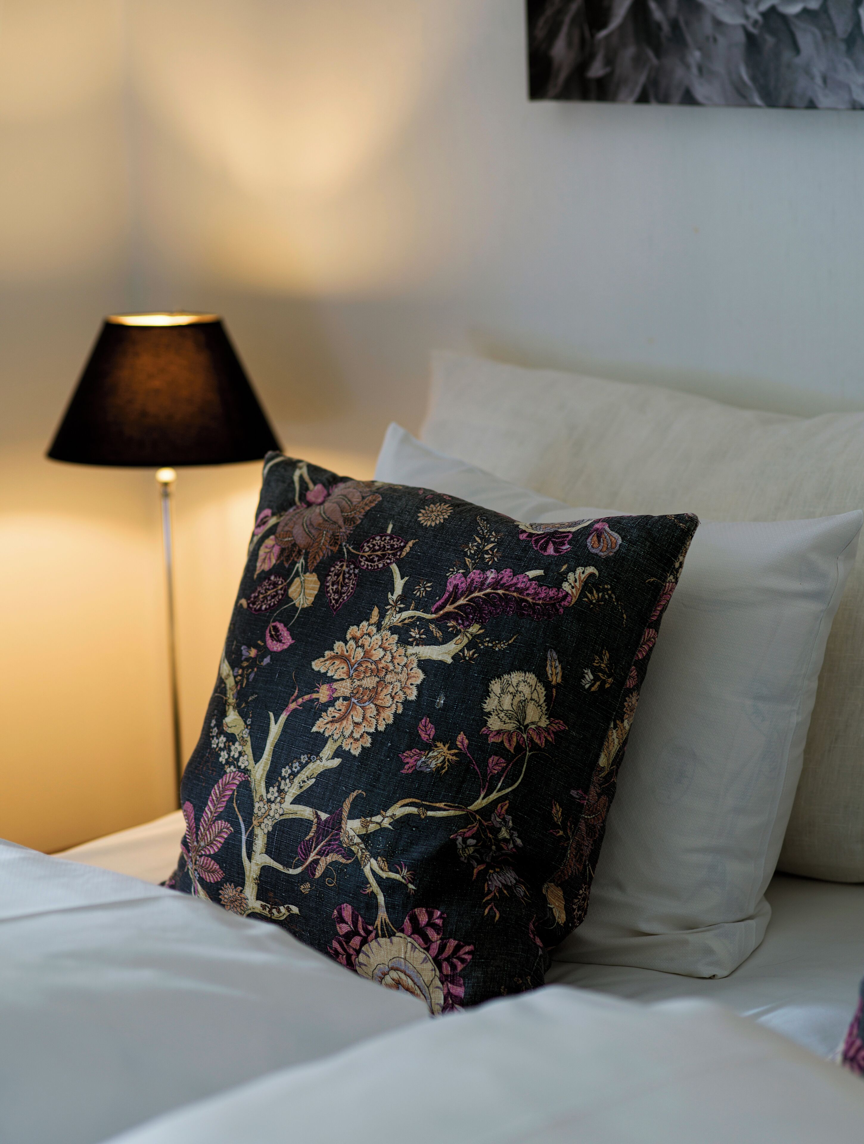 Un letto con biancheria bianca e un cuscino decorato con motivi floreali.