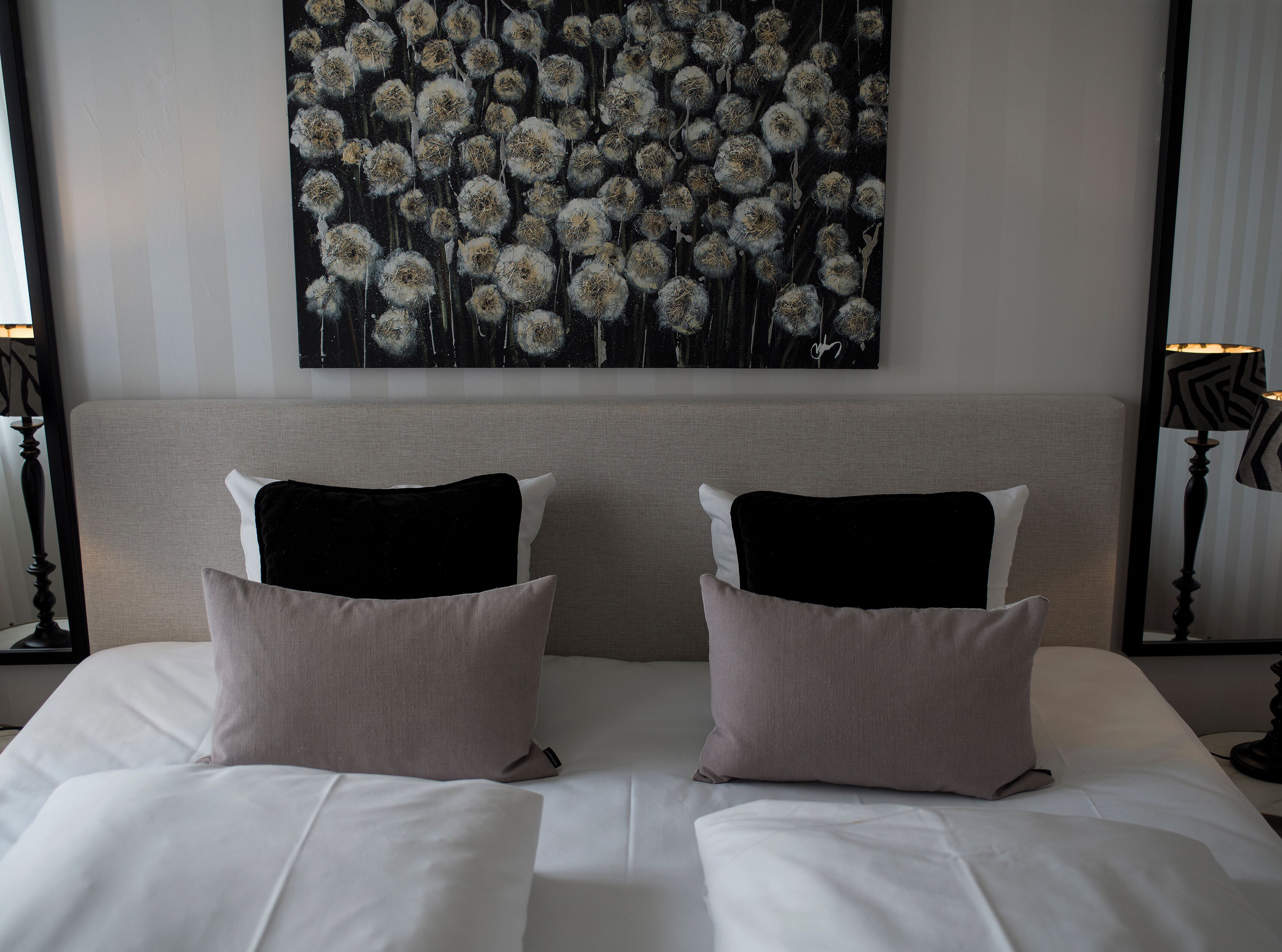A hotel room with a large bed, two pillows, a headboard, and a wall-mounted artwork.