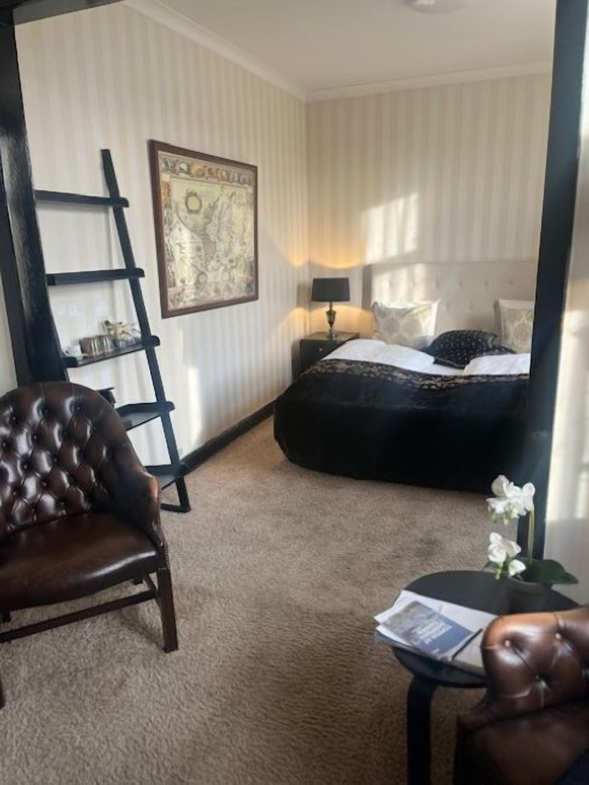 A hotel room with a bed, a chair, a small table, and a ladder against the wall.