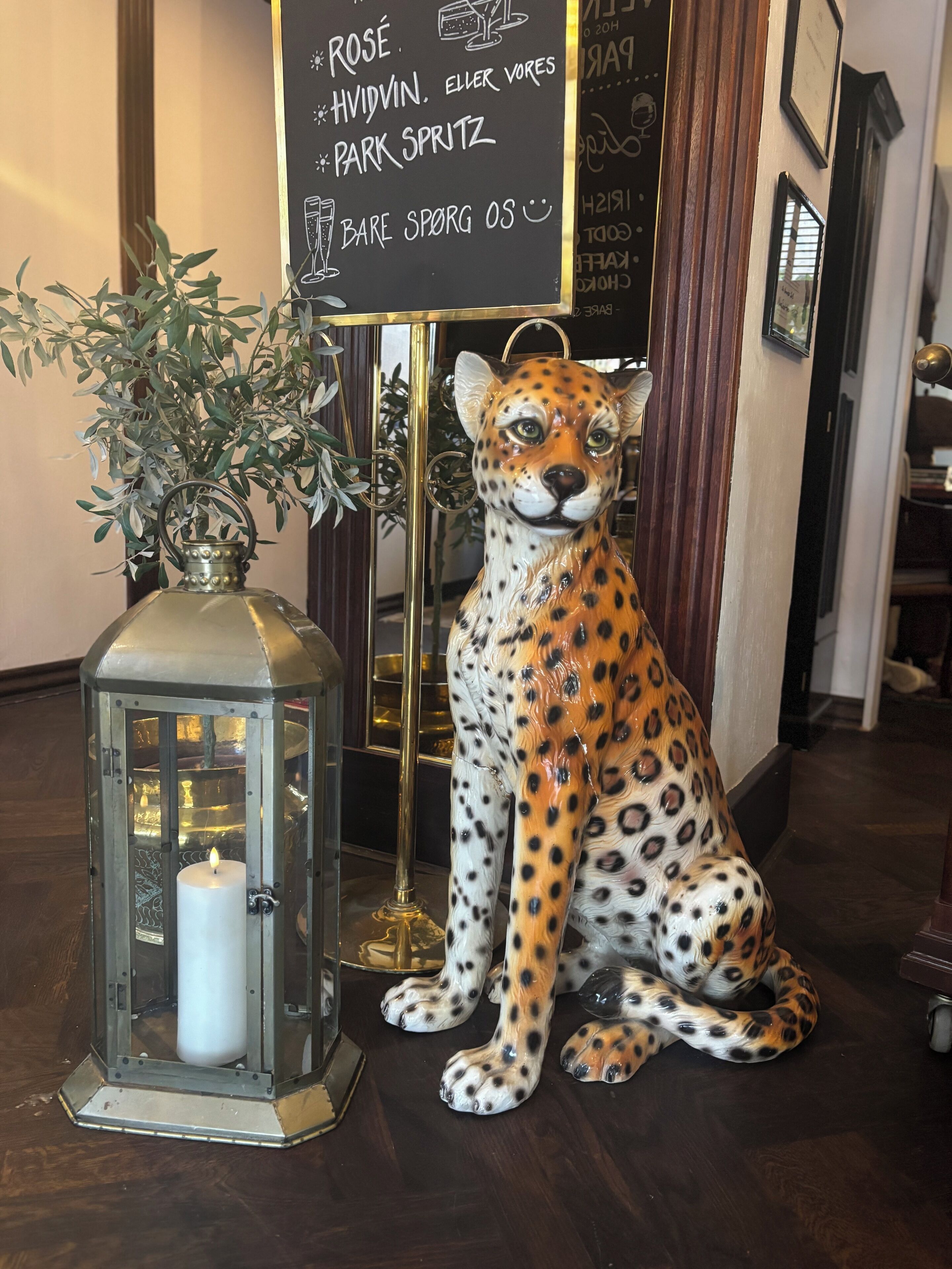 A leopard statue, a lit candle in a lantern, and a menu board with food items.
