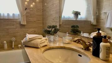 A bathroom with a marble sink, a bathtub, and a window with a plant.