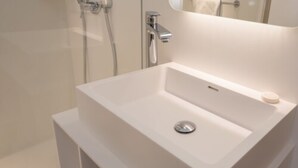 Un baño moderno con lavamanos blanco, espejo y ducha.