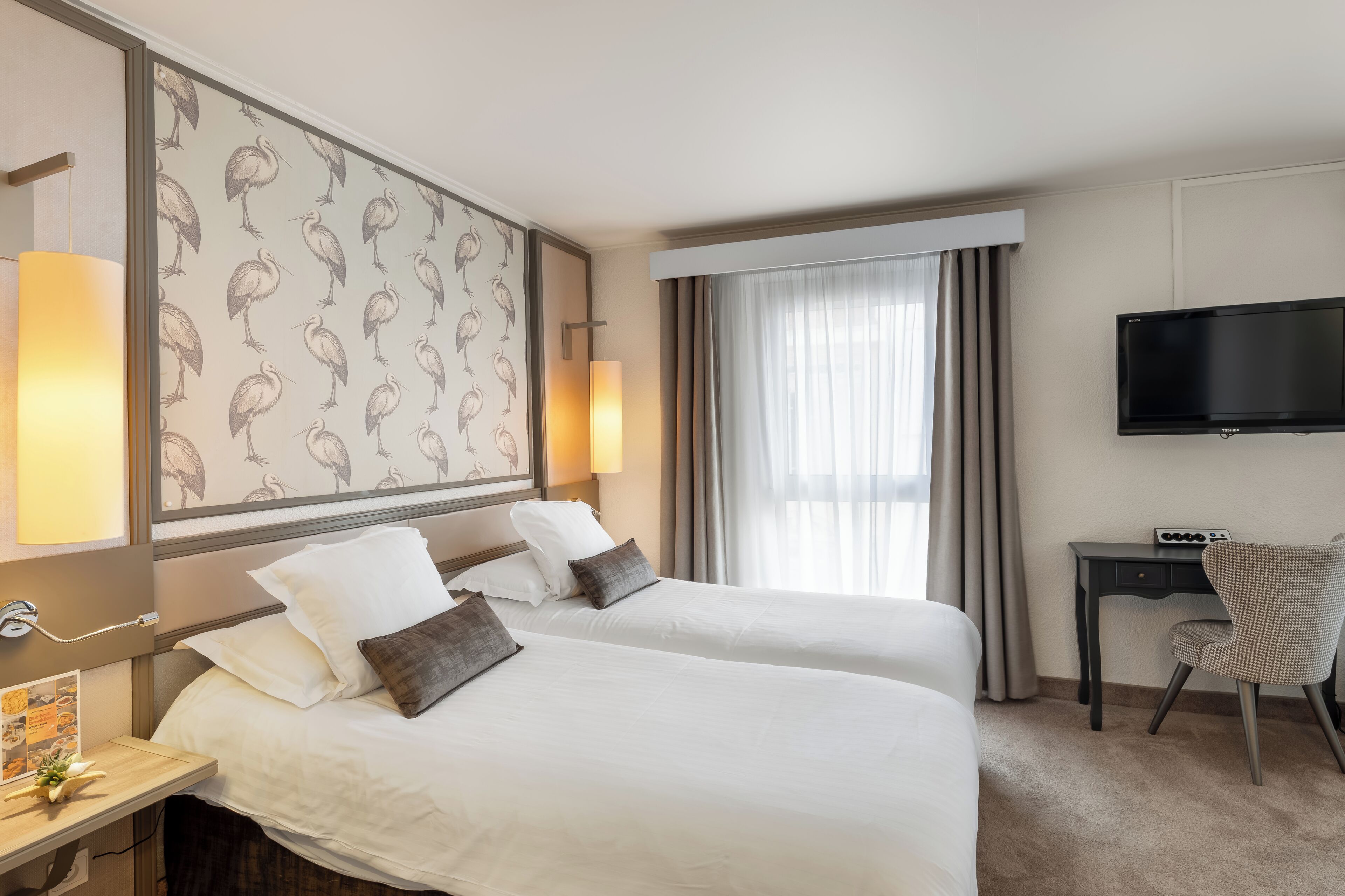 Une chambre d’hôtel avec deux lits, un bureau avec une chaise, un téléviseur à écran plat et une fenêtre avec des rideaux.