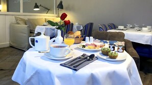 Un desayuno con una cafetera, tazas, un plato de comida y un florero con una rosa roja.