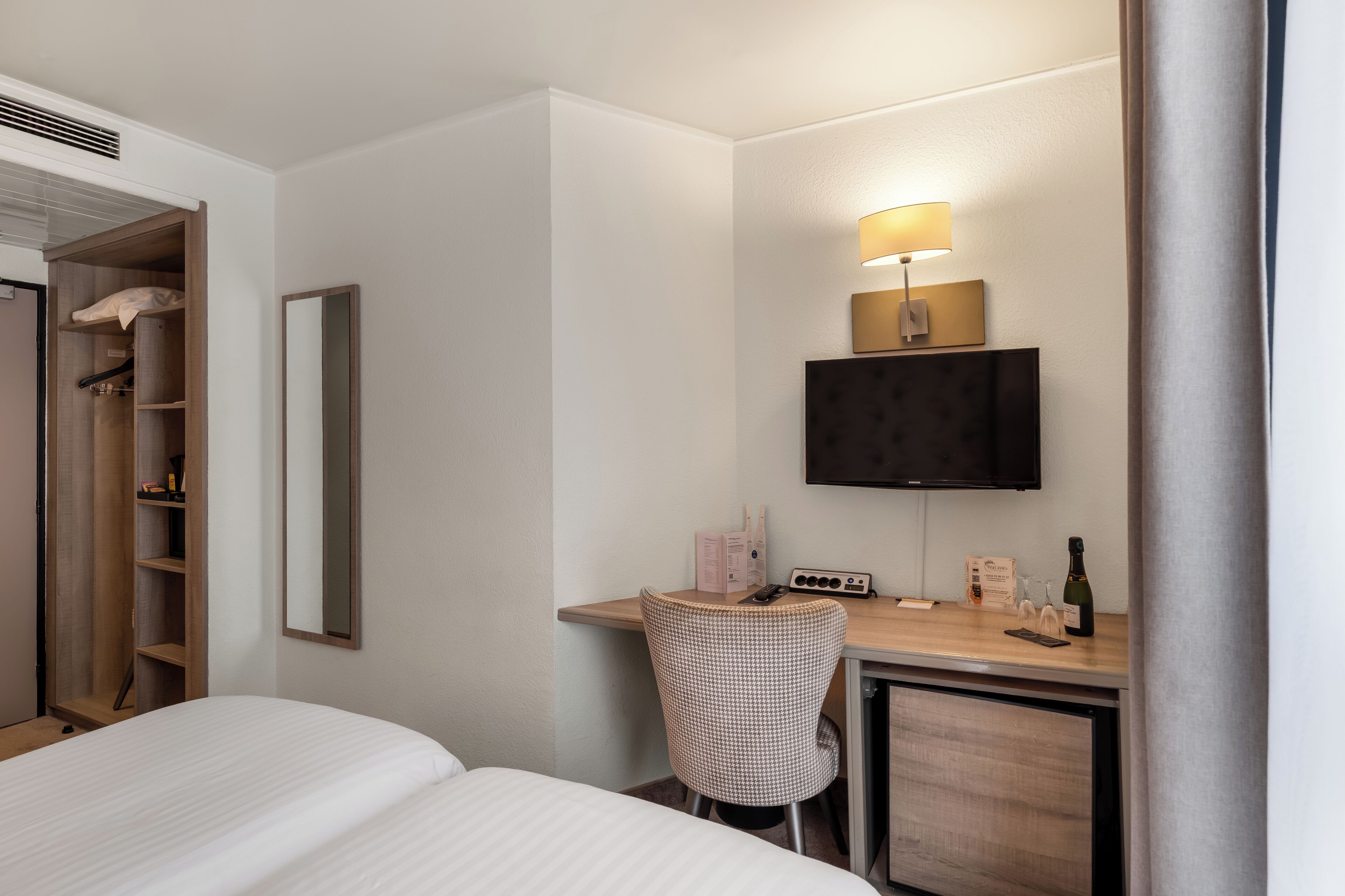 Ein Hotelzimmer mit einem Bett, einem Schreibtisch mit Lampe, einem Fernseher und einem Kleiderschrank.