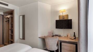 Ein Hotelzimmer mit einem Bett, einem Schreibtisch mit Lampe, einem Fernseher und einem Kleiderschrank.