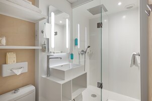 Een moderne badkamer met een douche in een glazen cabine, een witte wastafel en een spiegel.