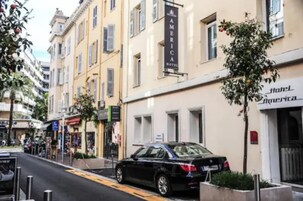 Straßenansicht mit einem schwarzen Auto, das vor einem Gebäude mit der Aufschrift 'Hotel America' geparkt ist.