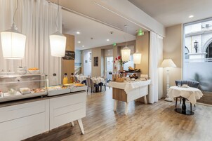 Un comedor de hotel con servicio de desayuno tipo buffet, mesas con manteles blancos y una variedad de opciones de comida.