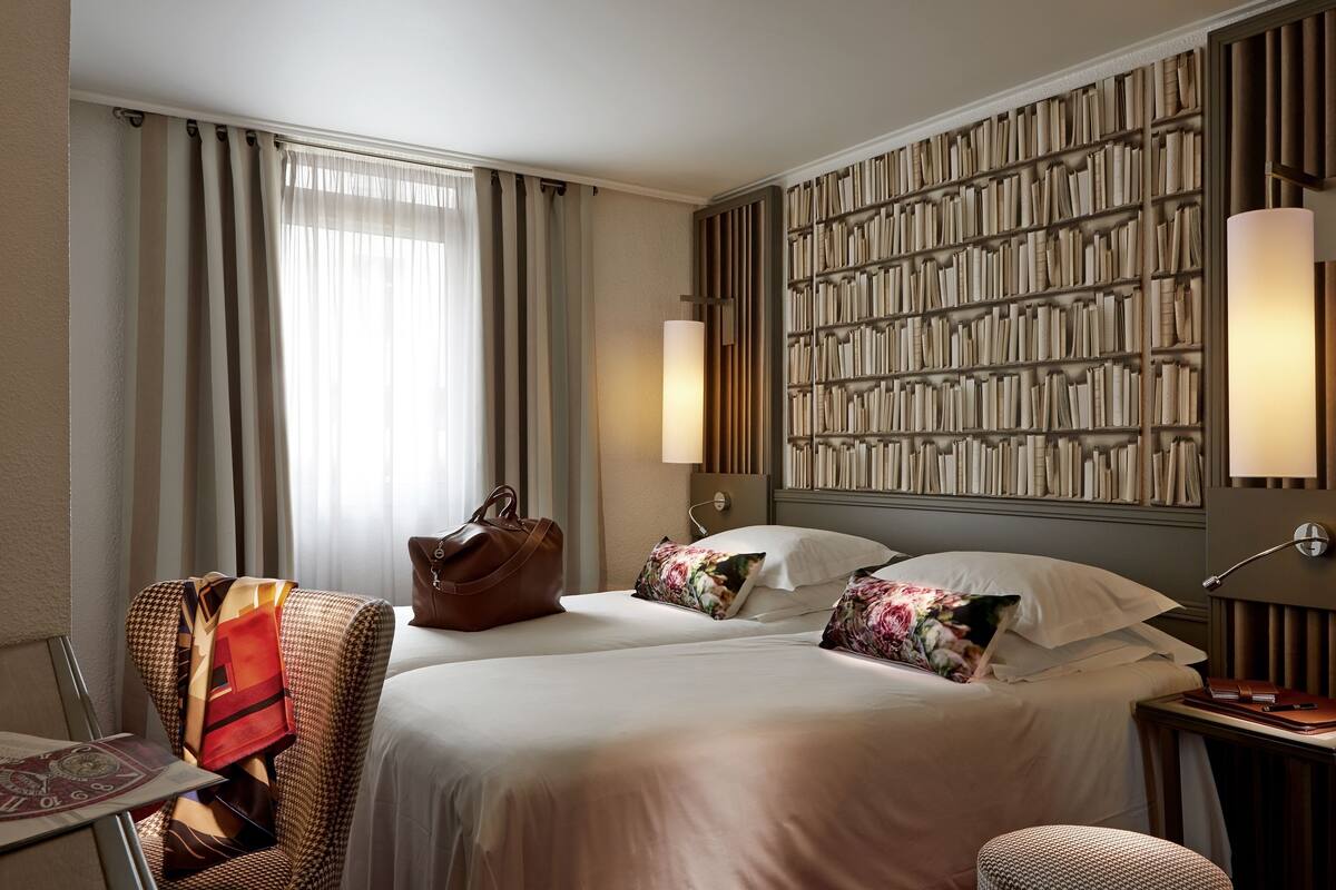 Une chambre d’hôtel avec deux lits, une bibliothèque, un bureau et une chaise.