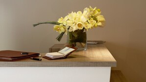 A reception desk with a vase of yellow flowers, a brown leather bag, and a notebook.
