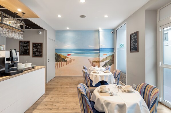 A restaurant with a beach mural, tables set for dining, and a coffee machine on the counter.