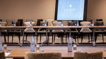 Una sala de conferències amb una taula llarga, cadires, ampolles d'aigua i una pantalla que mostra "L'EUROPE HOTEL RESTAURANT".