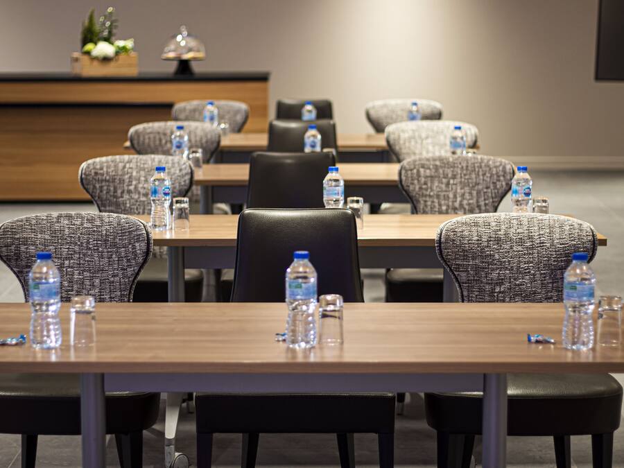 Un salón de conferencias con mesas, sillas, botellas de agua y una pantalla para proyector.