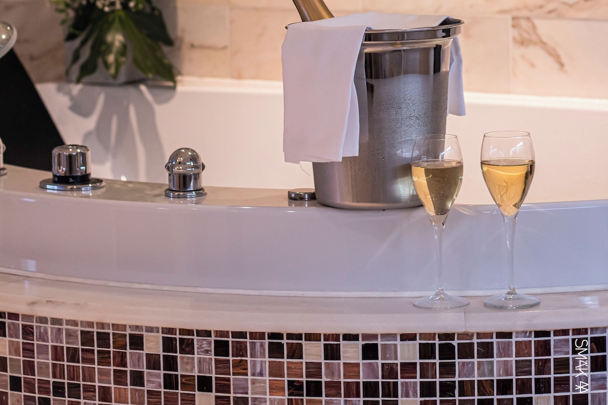 Een badkamer met een marmeren wand, een bloemstuk, een champagnefles en twee champagneglazen.