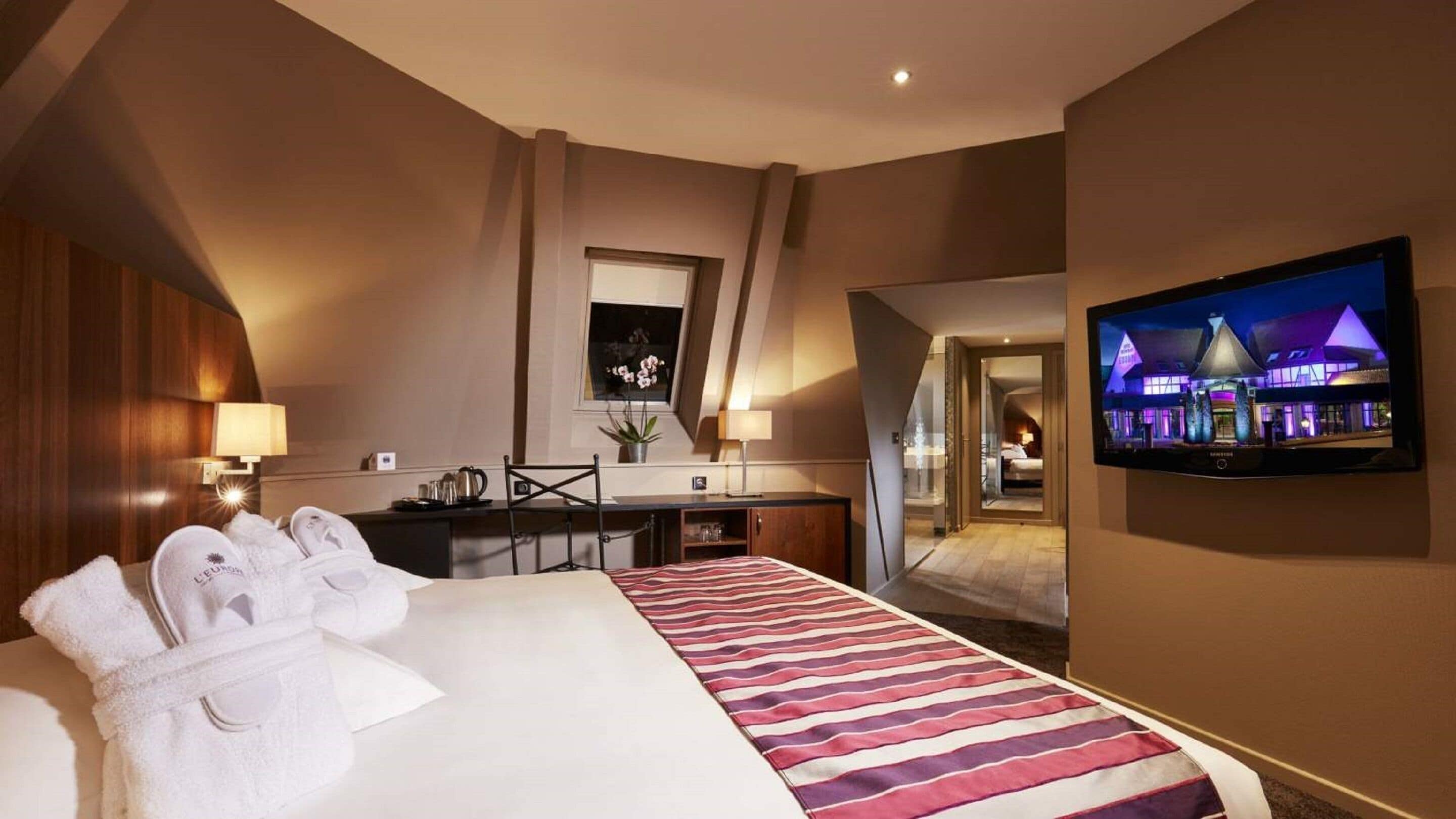 Ein Hotelzimmer mit einem großen Bett, einem Schreibtisch, einem Fernseher und Blick auf das Hotelgebäude.