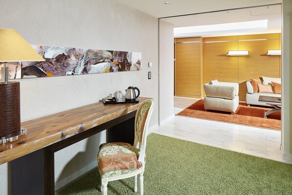A modern hotel room with a wooden desk, a green carpet, a white chair, and a large abstract painting on the wall.