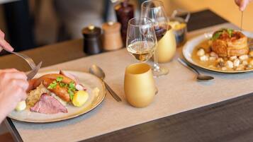 Una mesa de comedor con platos de comida, copas de vino y cubiertos.