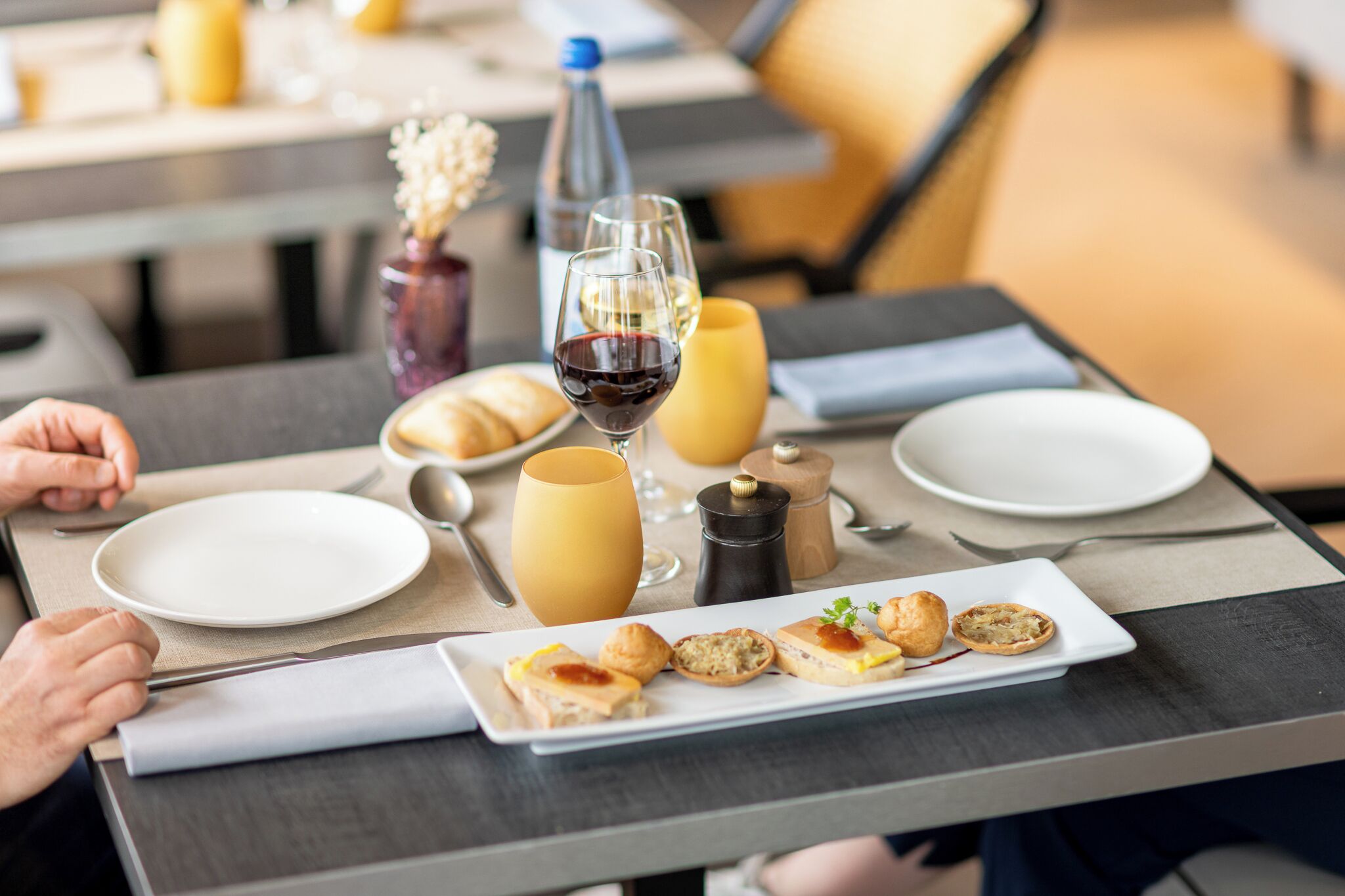 A breakfast setting with a plate of pastries, a glass of red wine, and a bottle of water on a table.