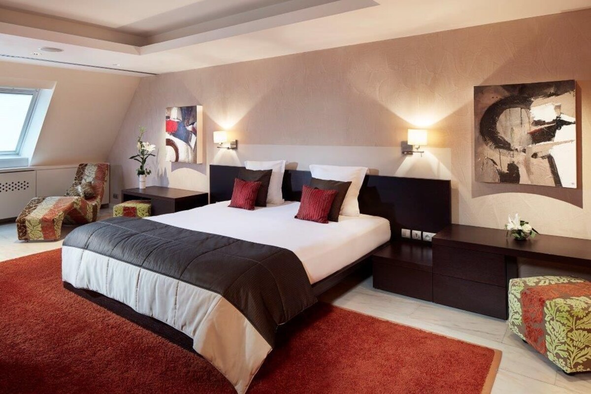 A modern bedroom with a large bed, two bedside tables, a nightstand, and a wall-mounted artwork.