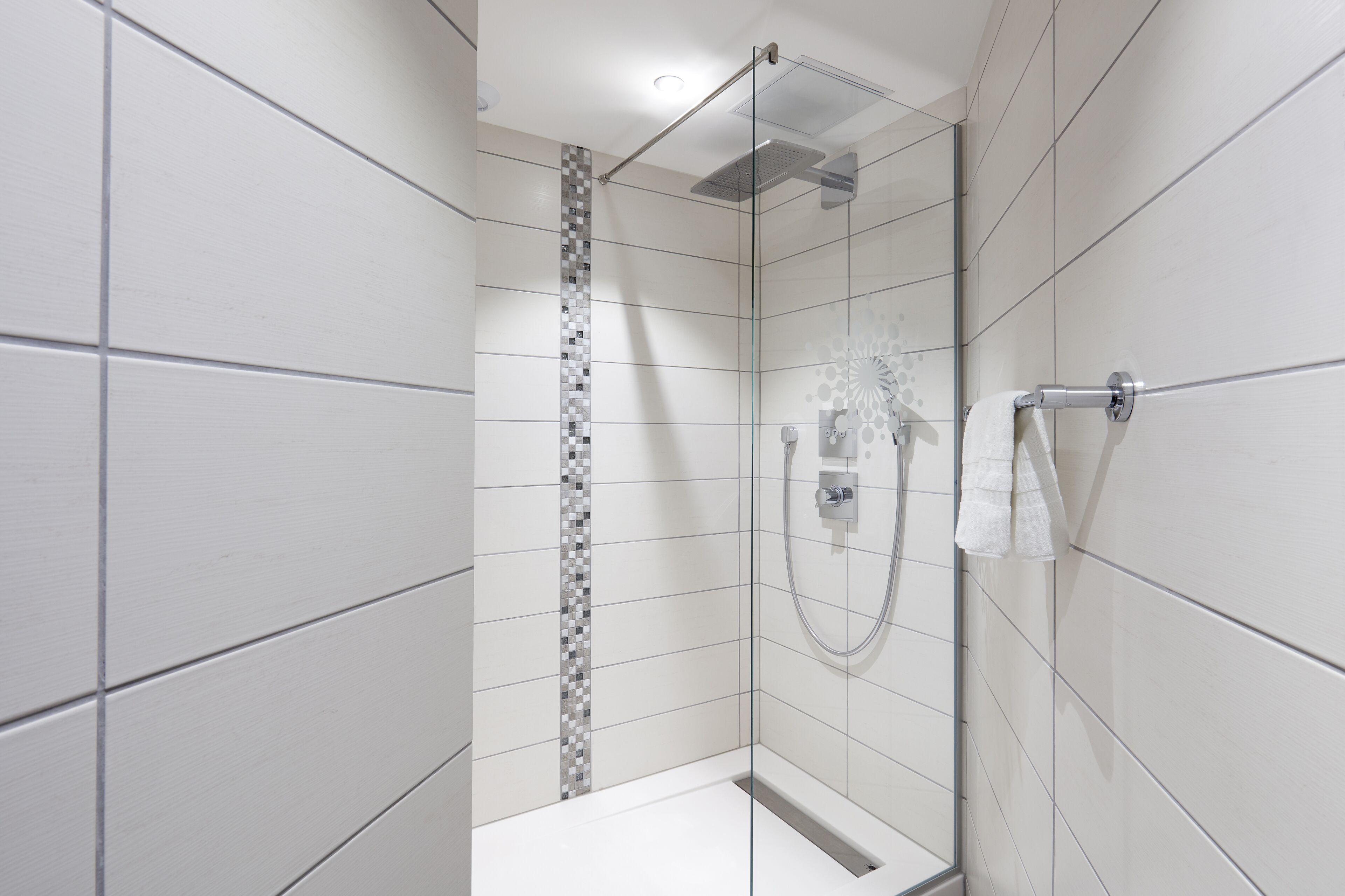 A modern shower with a glass door, a tiled wall with a decorative strip, and a towel rack.