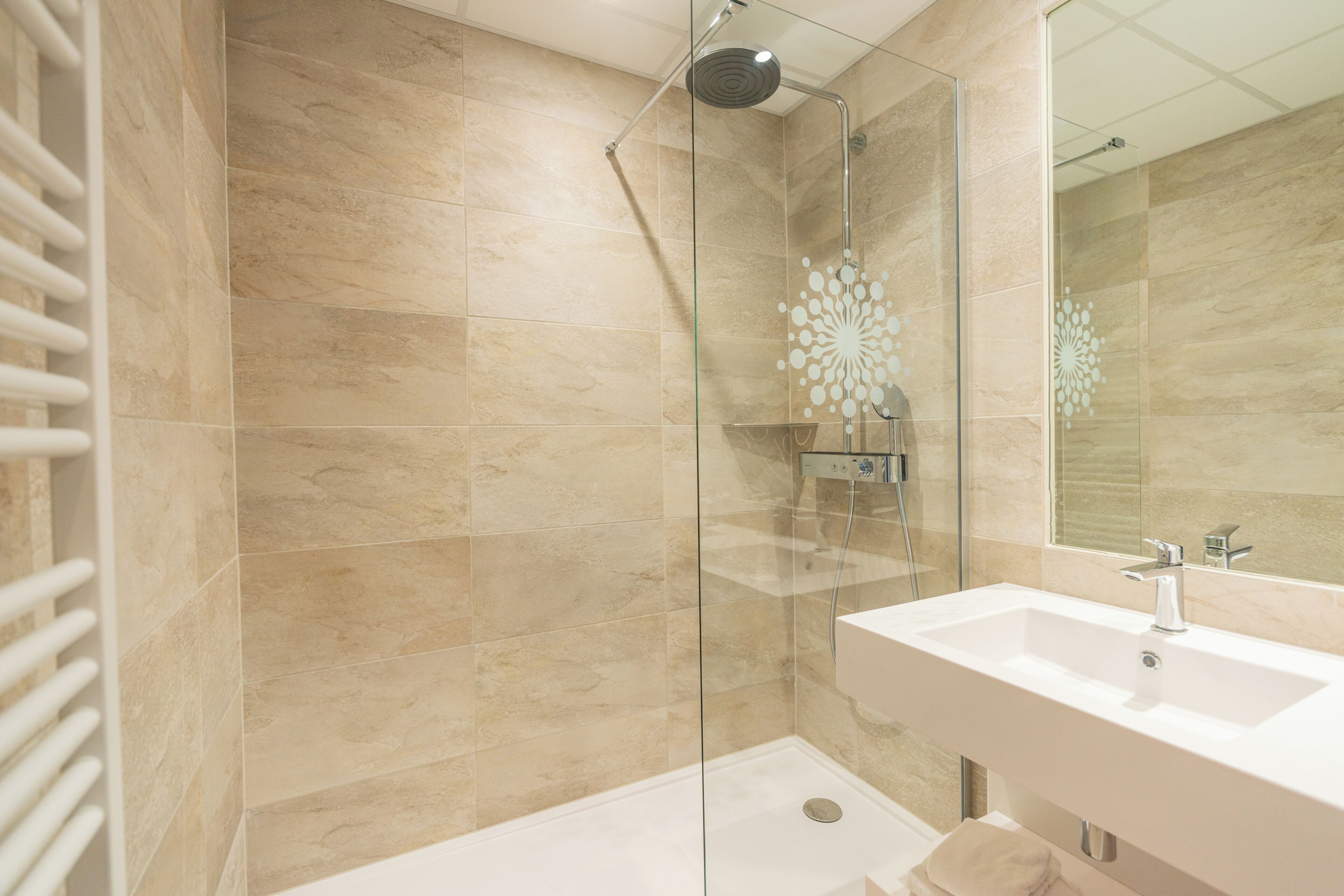 Een moderne badkamer met een douchecabine van glas, een wit wastafelmeubel en beige tegels.