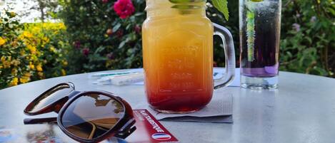 Una mesa con un jarro de té helado, un vaso de bebida morada y gafas de sol.