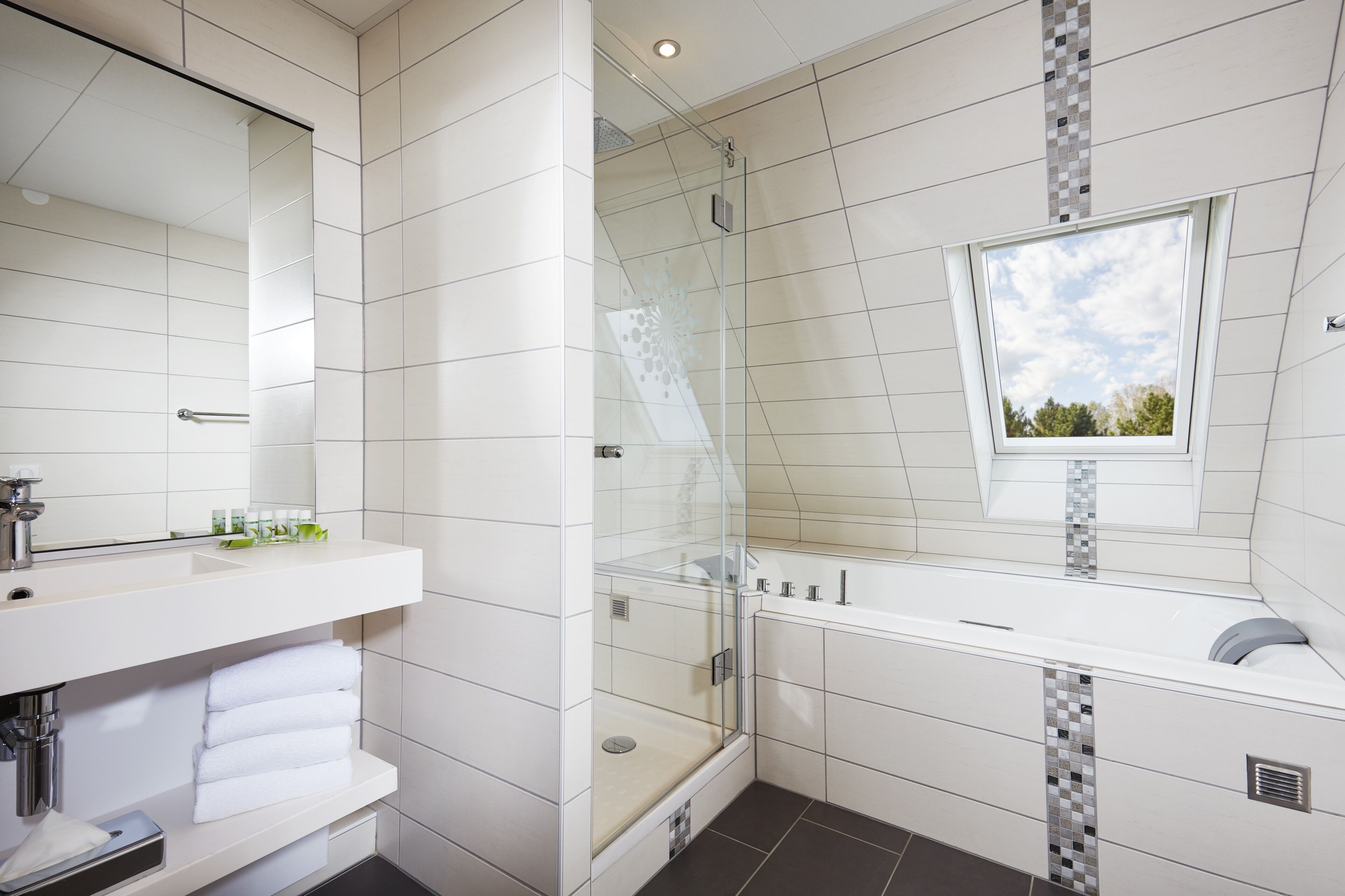 Un baño moderno con ducha envuelta en vidrio, un espejo grande y una ventana.