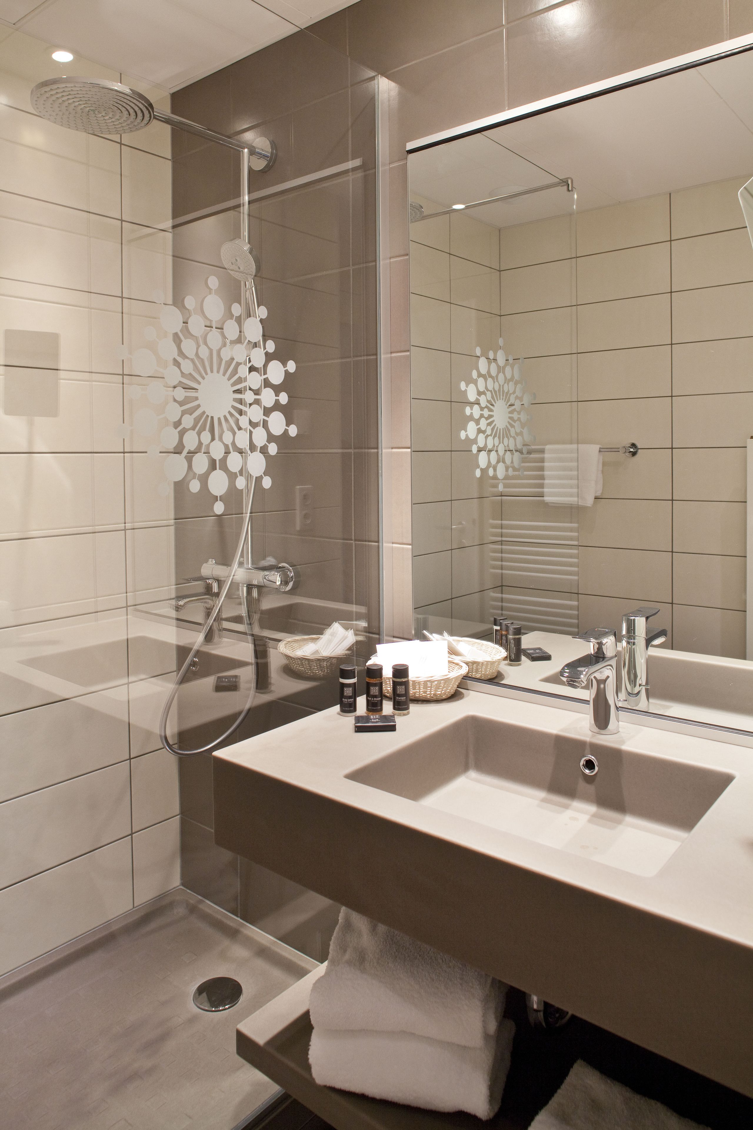 A modern bathroom with a large mirror, a shower with a unique circular design, and a vanity with a sink and toiletries.