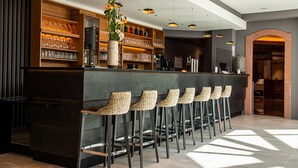 A bar area with a counter, bar stools, shelves with glassware, and a decorative vase with flowers. - Hotel L'Europe Colmar, BW Signature Collection (Horbourg-Wihr)