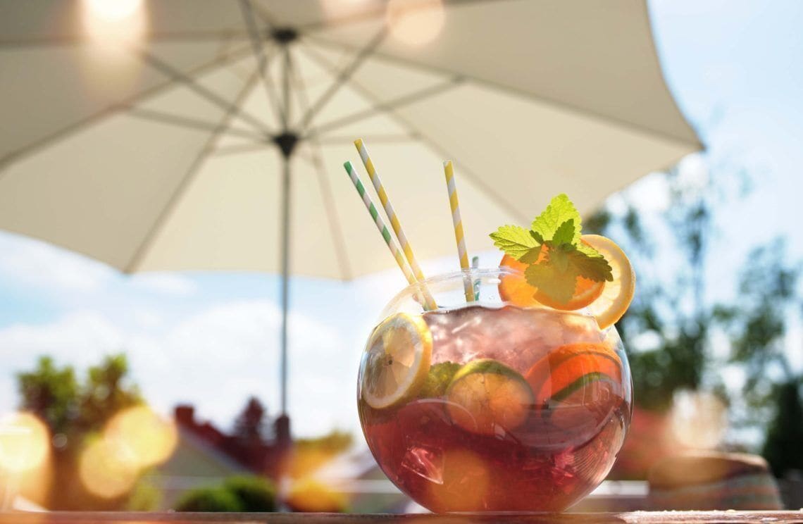 A clear glass with a drink, garnished with lemon slices and mint, under a white umbrella.