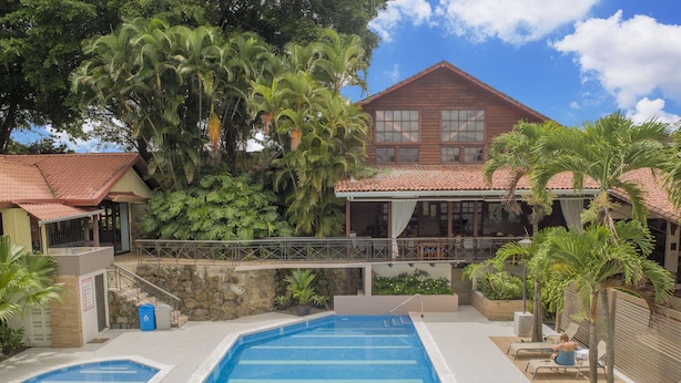 A pool area with two swimming pools, a covered seating area, and a building with a red roof. - El Rodeo Estancia Boutique Hotel & Steakhouse (San Rafael)
