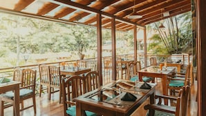 A restaurant with wooden tables and chairs, large windows, and a view of greenery. - El Rodeo Estancia Boutique Hotel & Steakhouse (San Rafael)