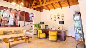 A spacious living area with a high wooden ceiling, a sofa, yellow chairs, a coffee table, and a desk with a plant. - El Rodeo Estancia Boutique Hotel & Steakhouse (San Rafael)
