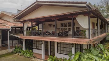 A two-story house with a balcony, a covered porch, and a garden with tropical plants.