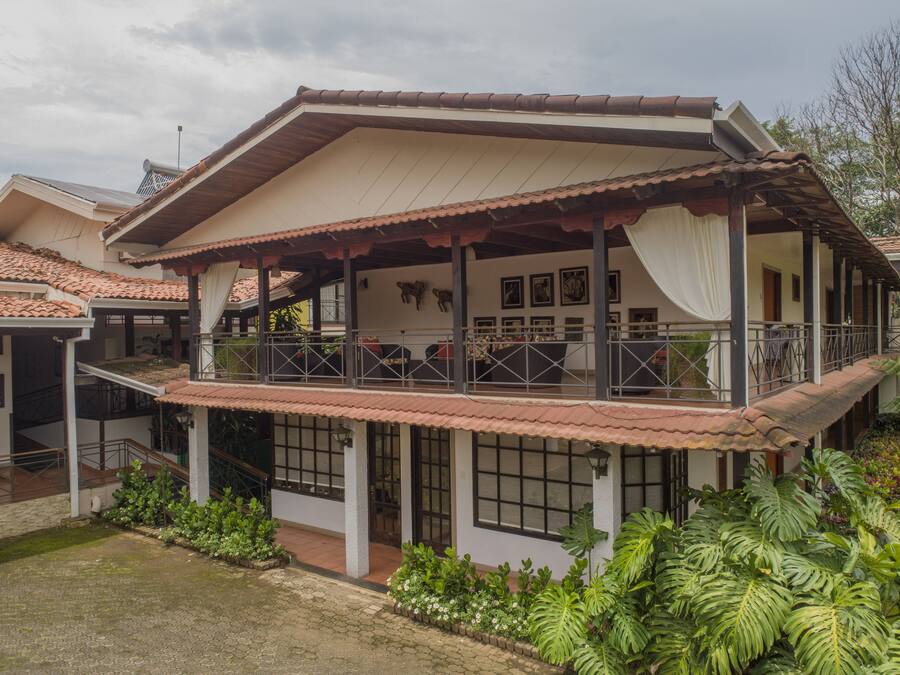 A two-story house with a balcony, a covered porch, and a garden with tropical plants.