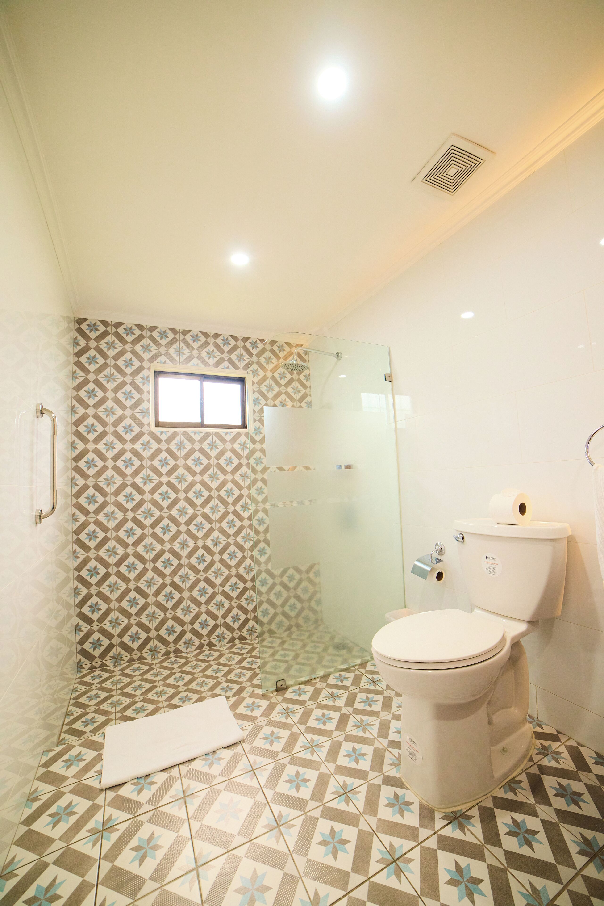 Un baño con azulejos estampados, inodoro, zona de ducha y ventana.