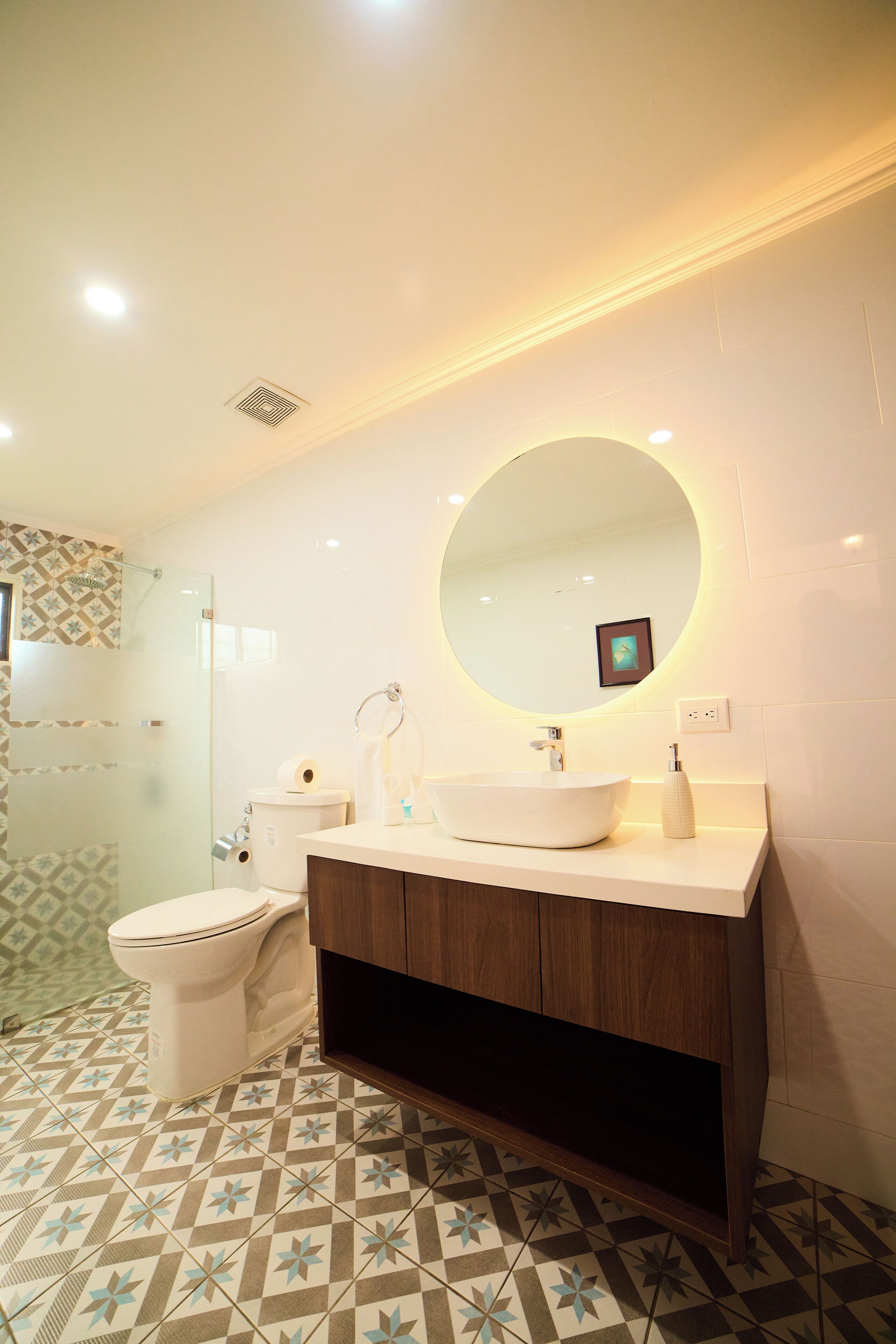 A modern bathroom with a round mirror, white sink, and a toilet.