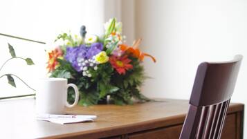 A wooden desk with a white mug, a small notepad, and a bouquet of flowers.
