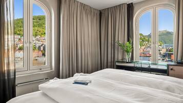 Une chambre d’hôtel avec un lit, un bureau et une vue sur la ville et les collines.