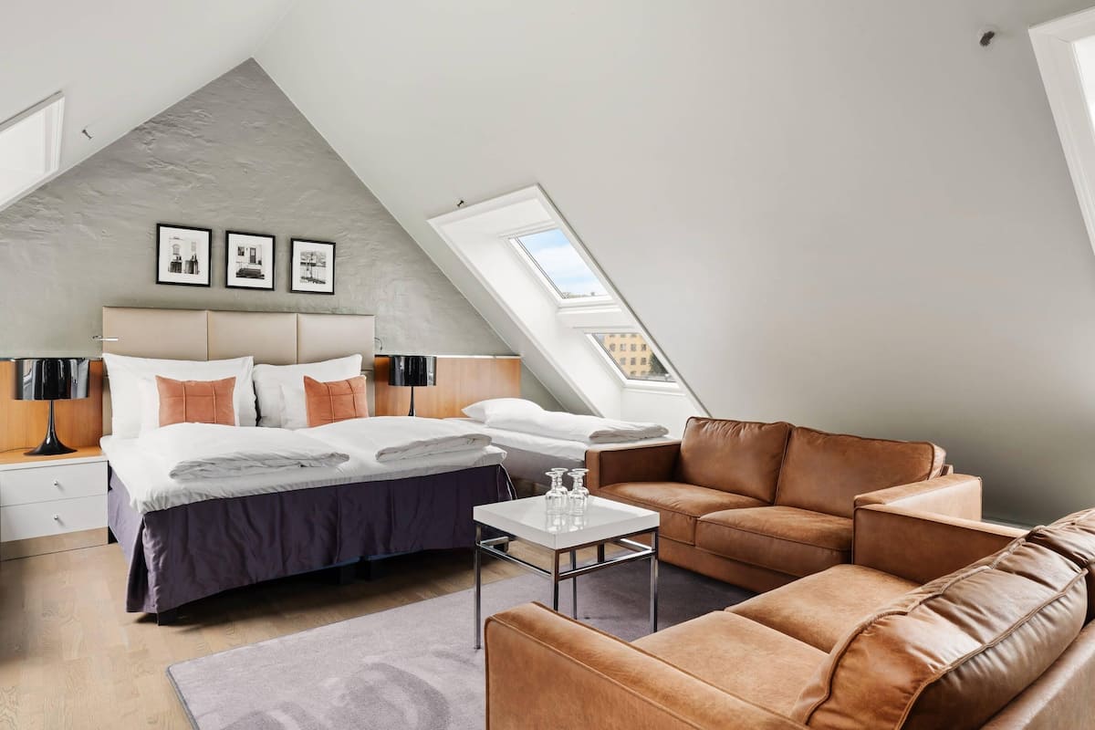 Quarto moderno com teto inclinado, uma cama, um sofá e uma mesinha.
