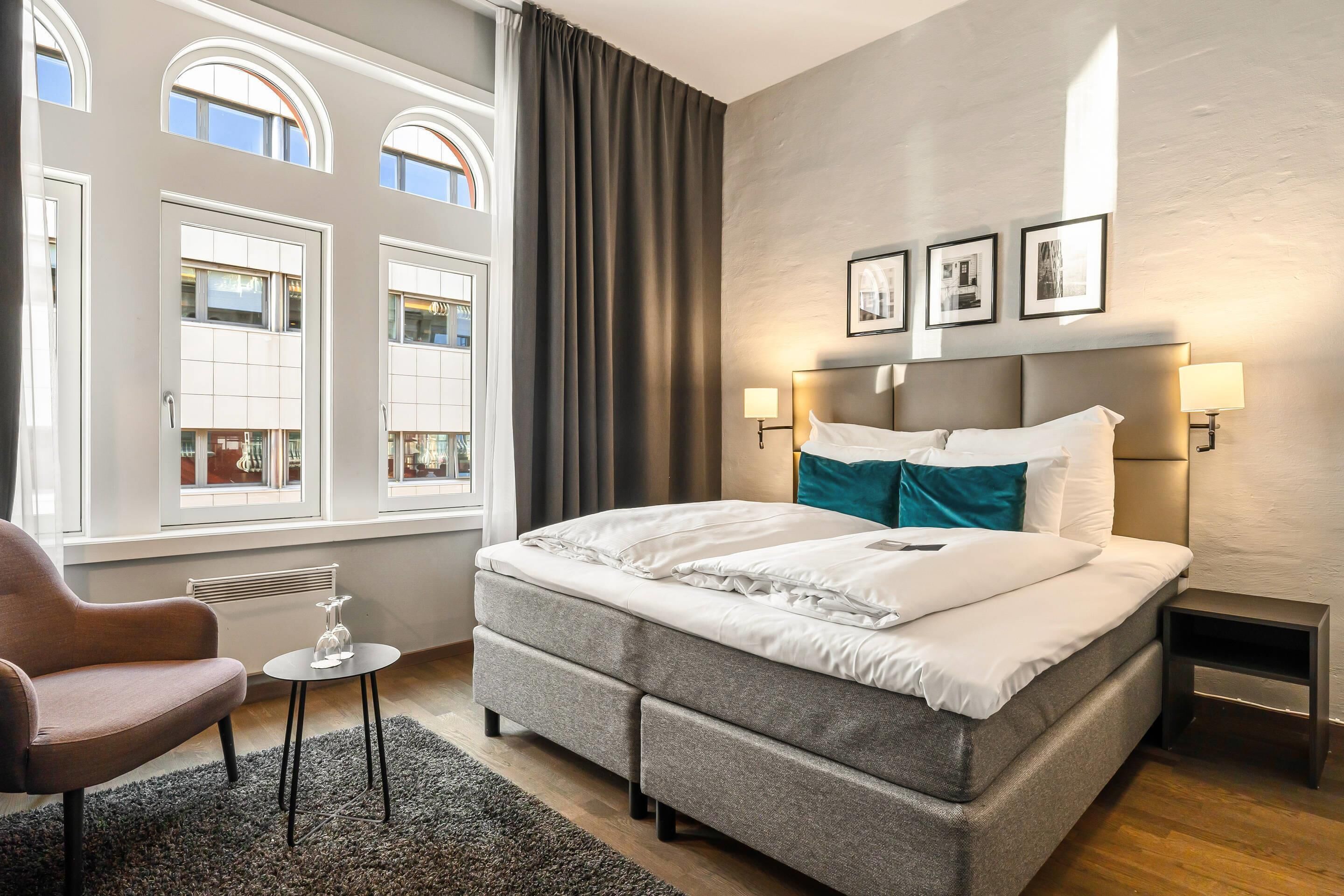 Una habitación de hotel moderna con una cama grande, dos lámparas de noche, una mesita con un vaso y una silla.